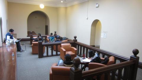 Two groups of 3 to 4 arm chairs separated by heavy wooden railing with two arched doorways behind