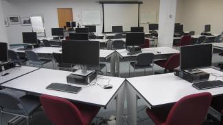 "View of the instruction lab desks and front screens from the back of the room"