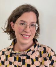 Woman with chin length light brown hair and glasses smiling at the camera